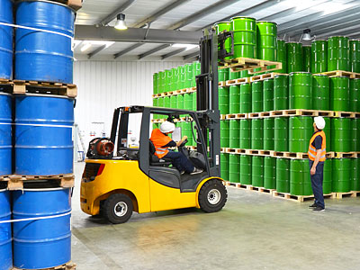 Gabelstapler in einem Lagerhaus, das grüne und blaue Fässer lagert.