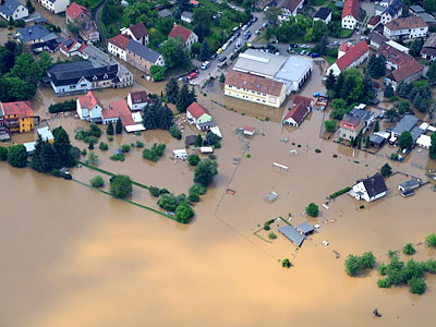 Überschwemmte Wohngegend mit Häusern und Straßen, die teilweise unter Wasser stehen.