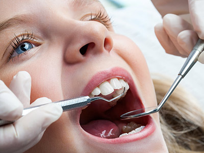 Ein Zahnarzt untersucht das Gebiss eines Kindes mit zahnärztlichen Werkzeugen.