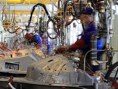 Fabrikhalle mit Arbeitern, die an Maschinen arbeiten und Funken erzeugen.