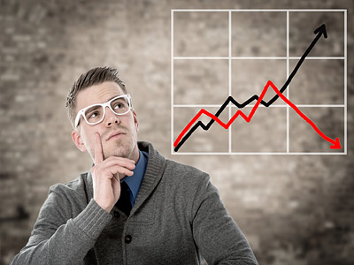 Eine nachdenkliche Person in einer grauen Strickjacke schaut auf ein Diagramm mit steigendem und fallendem Trend.