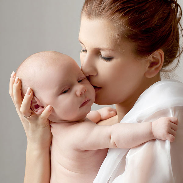 Eine Mutter küsst ihr Baby, das sie sanft im Arm hält.