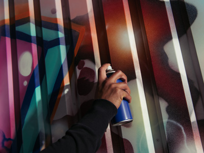 Eine Hand hält eine Spraydose vor einer bunten Graffiti-Oberfläche.