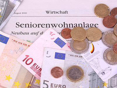 Geldscheine, Münzen und eine Zeitung mit dem Titel "Wirtschaft" und dem Thema "Seniorenwohnanlage".