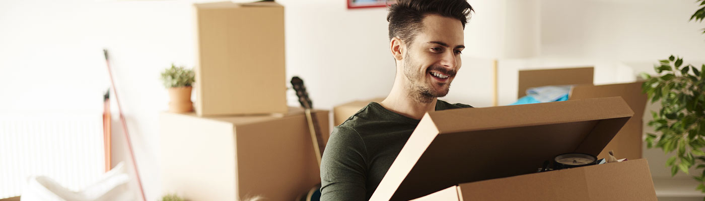Ein Mann schaut lächelnd in einen offenen Karton, umgeben von Umzugskartons.