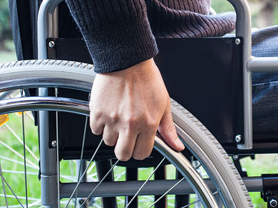 Eine Hand hält das Rad eines Rollstuhls.