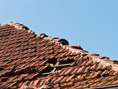 Das Bild zeigt ein beschädigtes Dach mit zerbrochenen Ziegeln vor blauem Himmel.