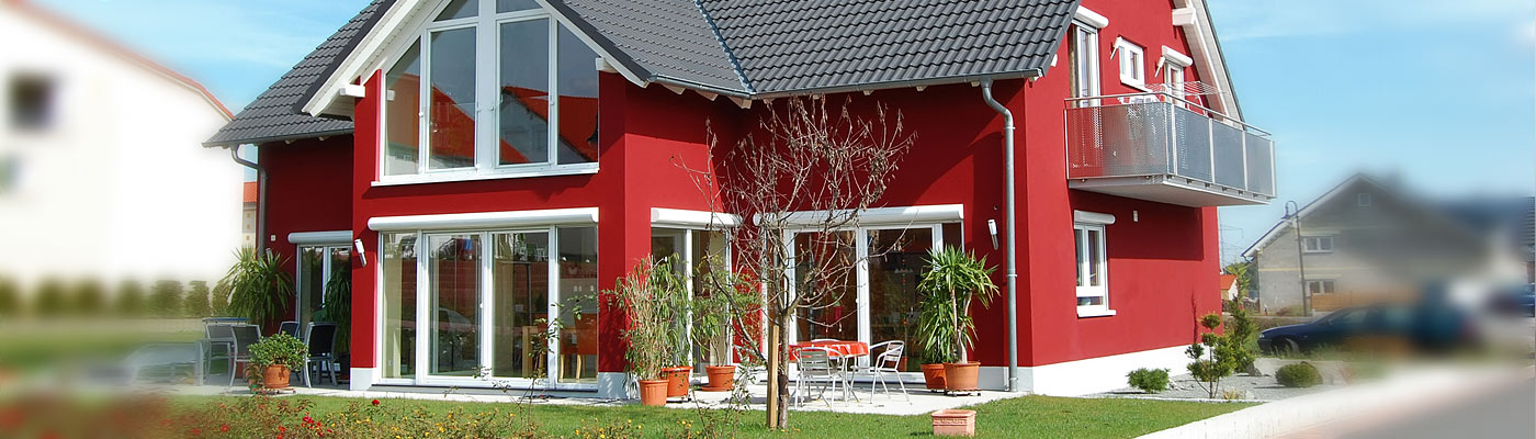 Ein rotes Haus mit großen Fenstern, einem Balkon und einem gepflegten Garten.