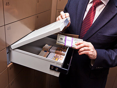 Ein Mann hält Geldscheine und schaut in ein Bankschließfach, das mit Bargeld gefüllt ist.