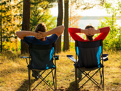 Zwei Personen sitzen entspannt in Campingstühlen und genießen die Aussicht auf einen See.