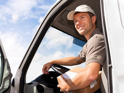 Ein Lieferfahrer sitzt im Fahrzeug und hält ein Paket in der Hand.