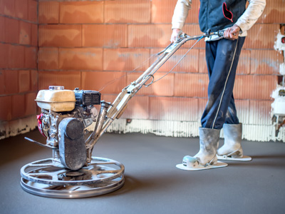 Eine Person benutzt eine Estrichmaschine auf frisch gegossenem Boden.