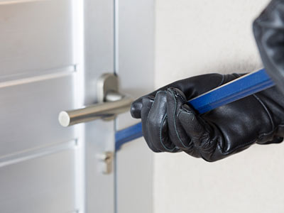 Eine Hand in einem schwarzen Handschuh, die mit einem blauen Werkzeug an einem Türschloss arbeitet.