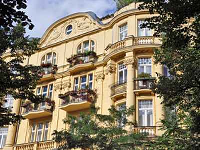 Eine gelbe Wohnhausfassade mit Balkonen und Blumenkästen, umgeben von Bäumen.