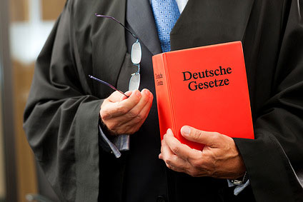 Ein Richter hält ein rotes Buch mit der Aufschrift "Deutsche Gesetze" und eine Brille in der Hand.