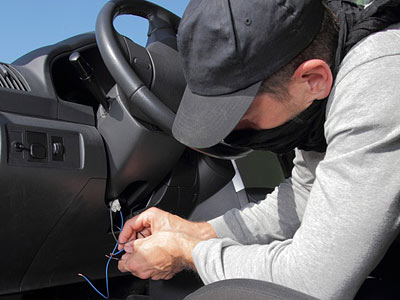 Eine Person mit einer Kapuze schraubt an den Kabeln im Innenraum eines Autos.
