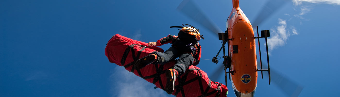 Ein Rettungshubschrauber hebt eine Person, die in einer roten Tragetasche hängt, in den Himmel.