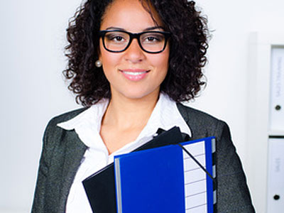Eine Frau mit Brille, die in einem Anzug gekleidet ist und Ordner in der Hand hält.